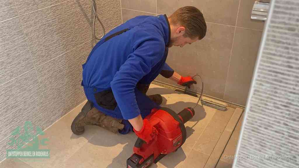 Een monteur ontstopt een langwerpige douchegoot met een elektrische veer, een doucheputje verstopt door haren en zeep in Berkel en Rodenrijs